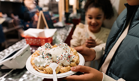 someone holding a funnel cake at the Enchant Christmas village food court