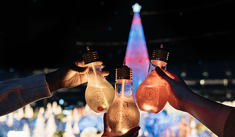 three light bulb glasses with drinks with the Enchant christmas tree view in the background