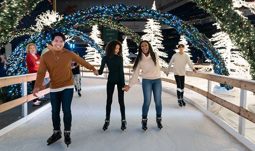 friends holding hands and skiing together at the ice skating area of the Enchant Christmas Village