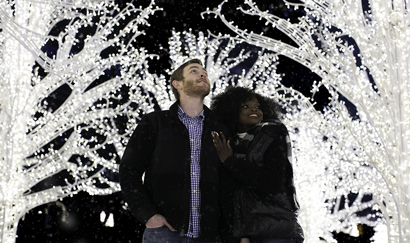 couple posing and smiling under lightened trees at the Enchant Christmas village