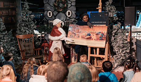 mrs claus is showing the kids some photos from a book at the little elves play place at the Enchant Christmas village