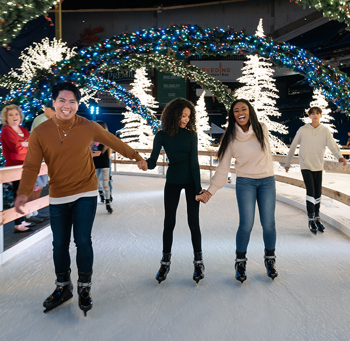 friends holding hands and ice skating at enchant christmas village