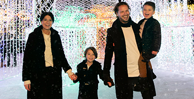 family of four holding hands in front of Enchant Christmas Village lights