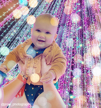 person holding a baby under the stripped Enchant Christmas lights
