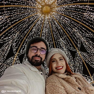 a couple is smiling under a light dome at the Enchant Christmas Village